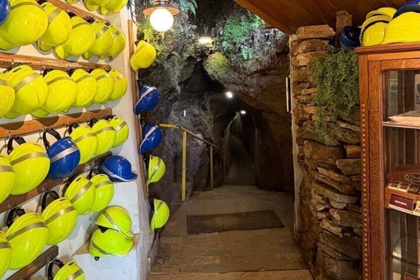A tunnel with helmets on display, a stone wall, and a wooden door. 4