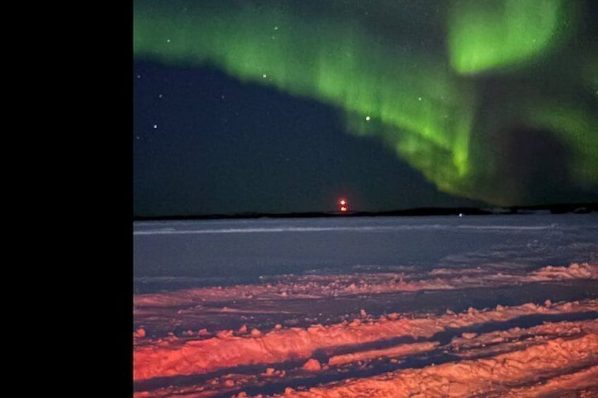 The Northern Lights over a snowy landscape with a distant light source. 3
