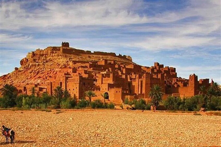 A large, ancient stone fortress on a hill with palm trees in the foreground. 5