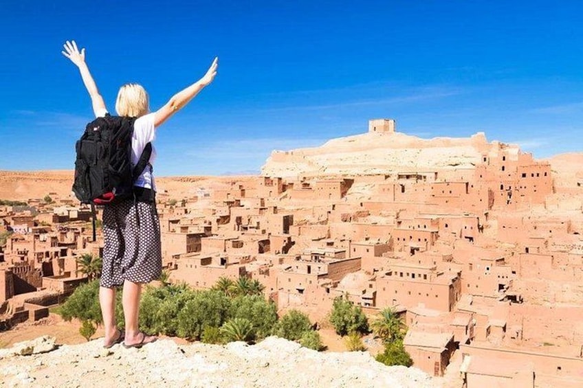 A person with arms raised, overlooking a densely packed village with traditional architecture. 1