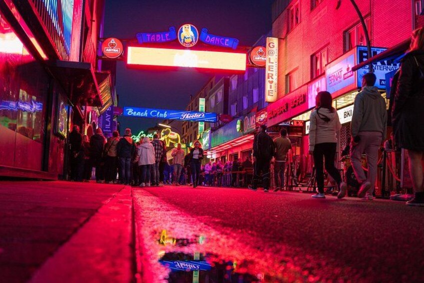 A neon-lit street with people standing in line at various establishments. 3
