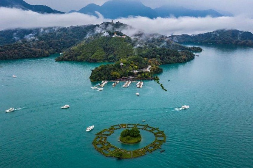 A lake with boats, a floating bridge, and a forested island with a building. 3