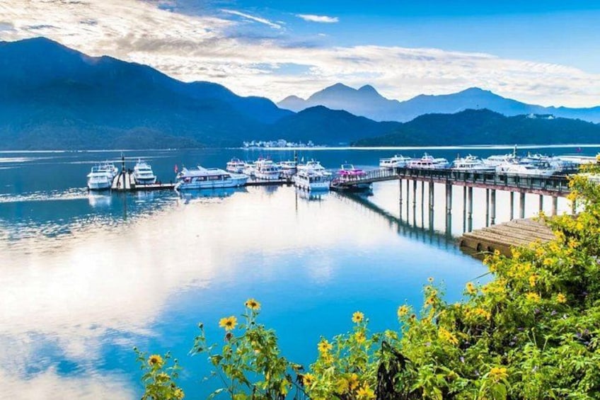 A marina with boats docked, a pier extending into calm water, and mountains in the background. 4