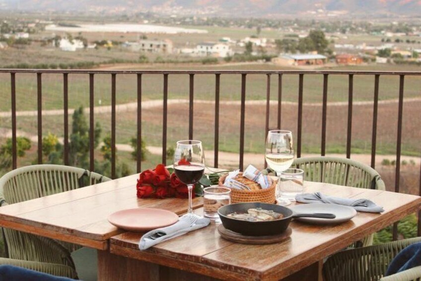 A wooden table set outdoors with a view of a vineyard and distant buildings. 4