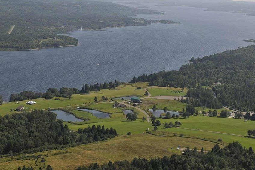 A coastal landscape with a large body of water, green fields, and scattered buildings. 3