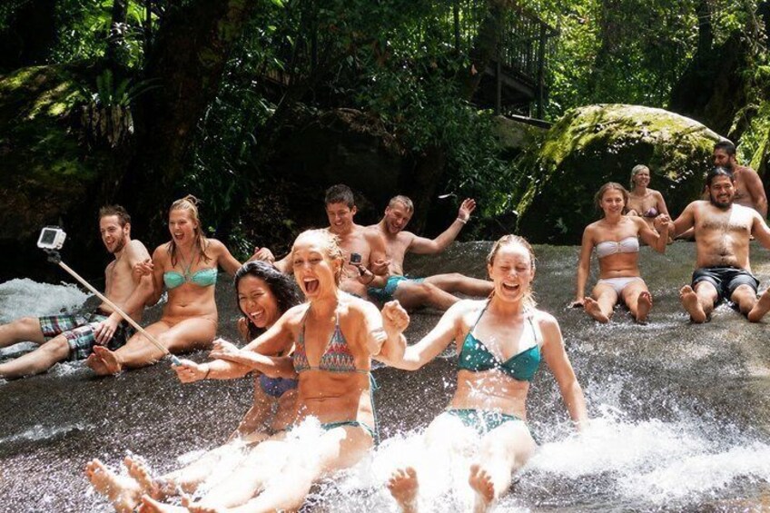 A group of people sitting on a wet surface, possibly a river or pool, surrounded by greenery. 4