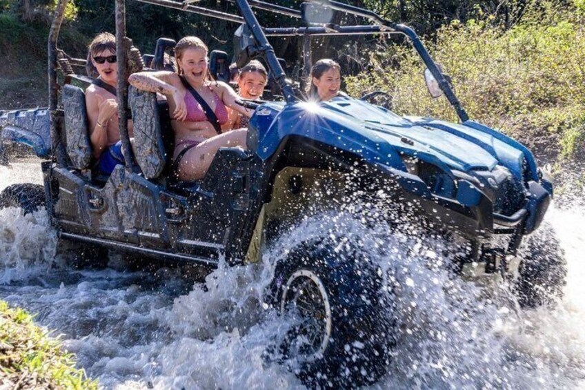 A blue off-road vehicle with four passengers driving through a water body. 2