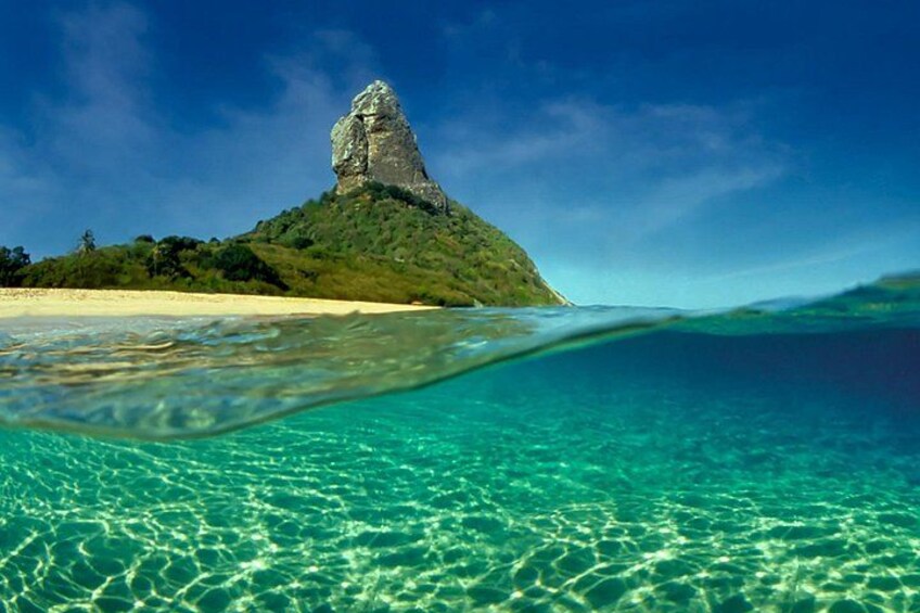 Une mer d’un bleu profond, une plage de sable et une colline rocheuse couverte de végétation. 2