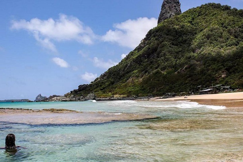 Una playa con agua turquesa cristalina, una orilla arenosa y una colina verde con una imponente formación rocosa. 2