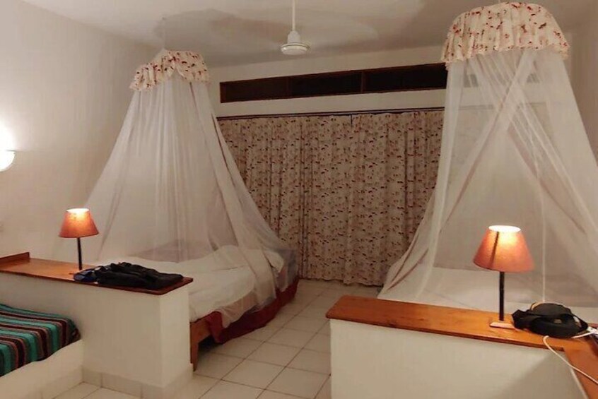 A bedroom with two beds, each with a canopy, and a bedside table with a lamp. 3