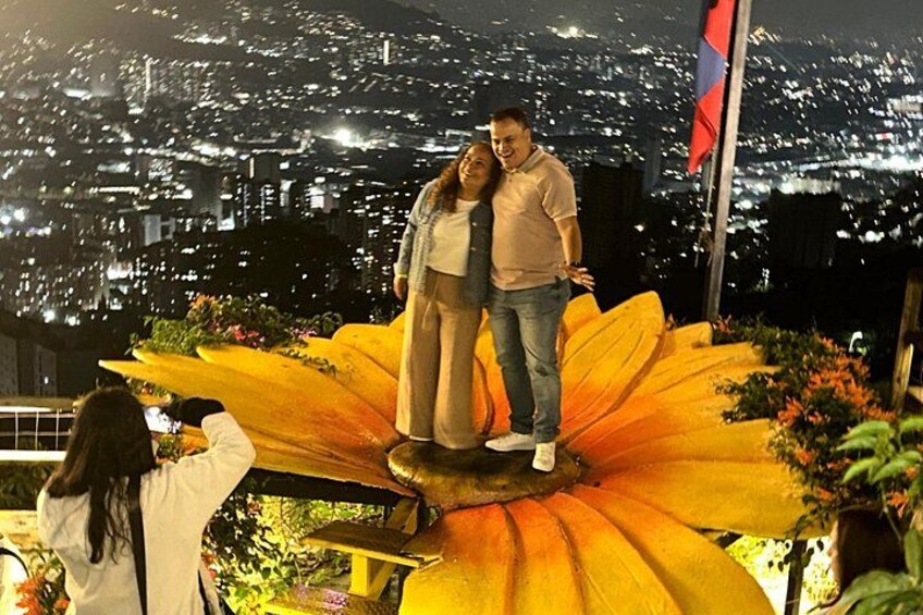 Una pareja de pie sobre una gran escultura floral, con un paisaje urbano de fondo. 1