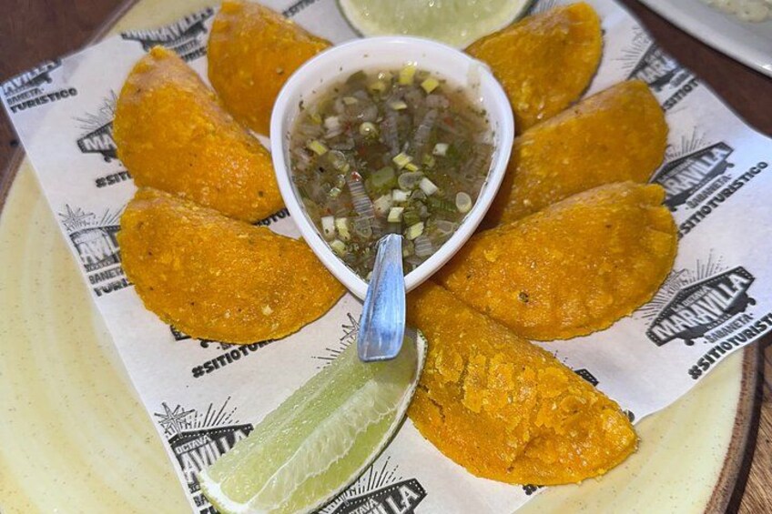 Un plato de antojitos dorados, un tazón pequeño de salsa verde y una cuña de lima. 4
