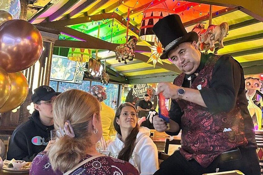 Una persona con bombín y chaleco realizando un truco de magia con una carta. 2