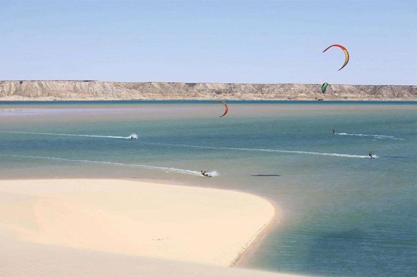 A beach with clear water, a sandy shore, and people kite surfing. 3