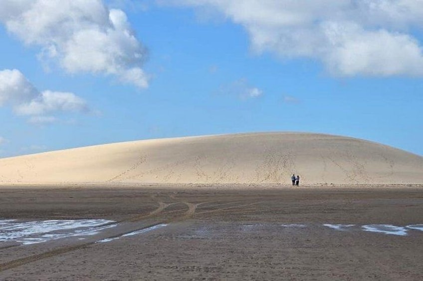 A large sand dune with two people walking on the beach. 2