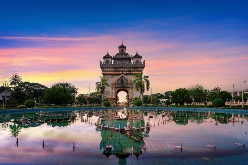 A historic gate with a reflection in a calm water body, surrounded by greenery and palm trees. 4
