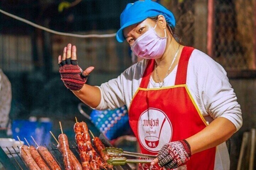 A street vendor grilling sausages and skewers, wearing a red apron and gloves. 2