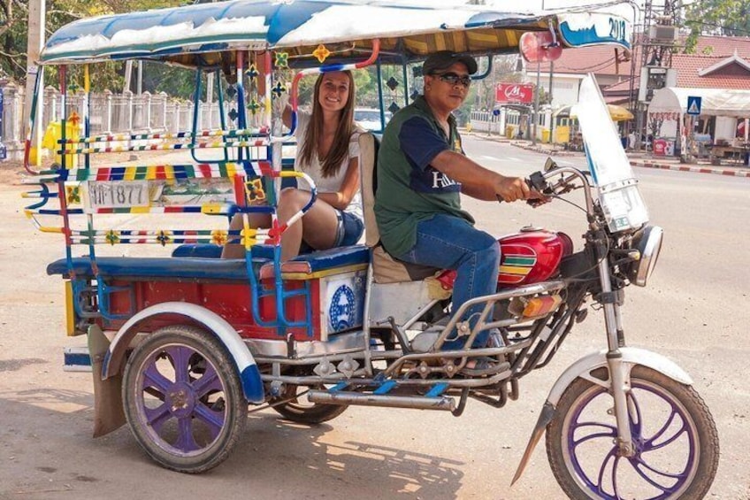 A colorful rickshaw with a man and a woman seated, driving on a street. 1
