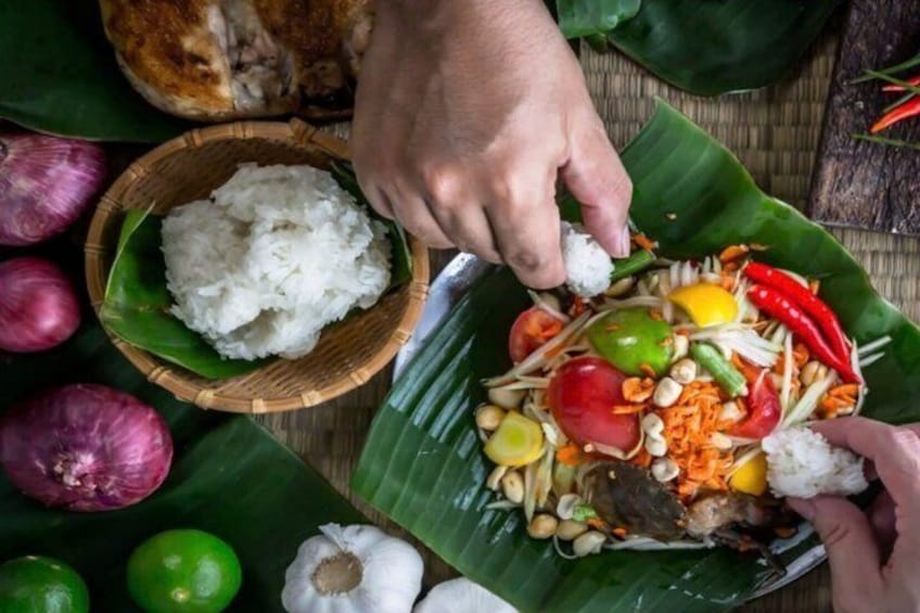 A person preparing a dish with rice and vegetables on a banana leaf. 3