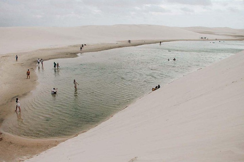 A desert landscape with a body of water, people walking and swimming, and sand dunes. 1