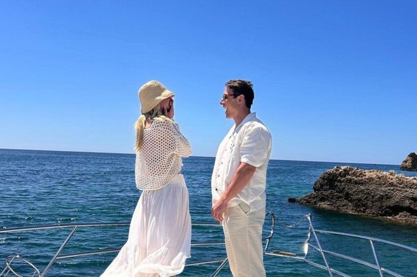 A couple standing on a boat with a rocky coastline in the background. 2
