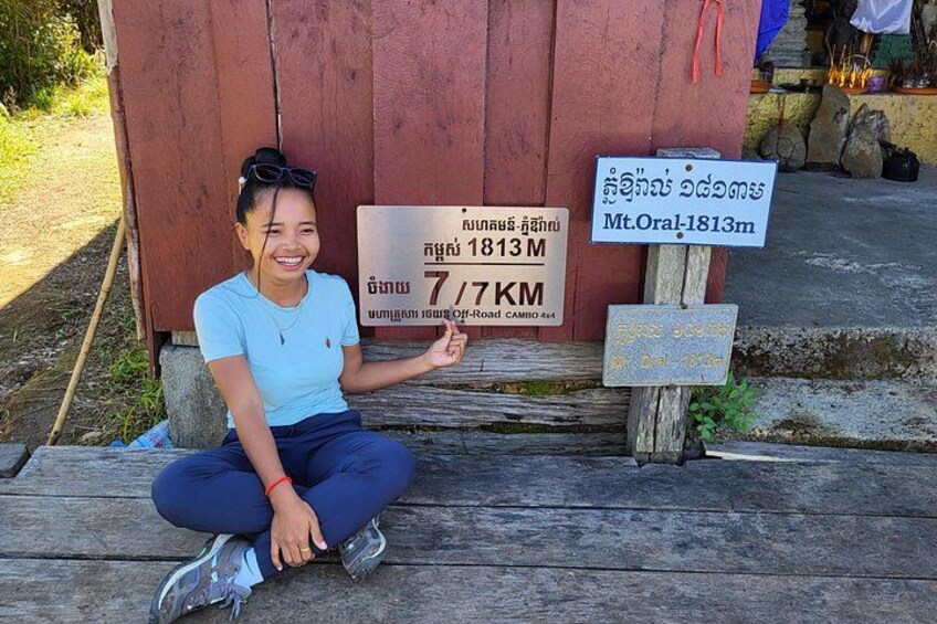 A person sitting on wooden steps with a sign indicating a height of 1813 meters and a distance of 7.7 kilometers. 4