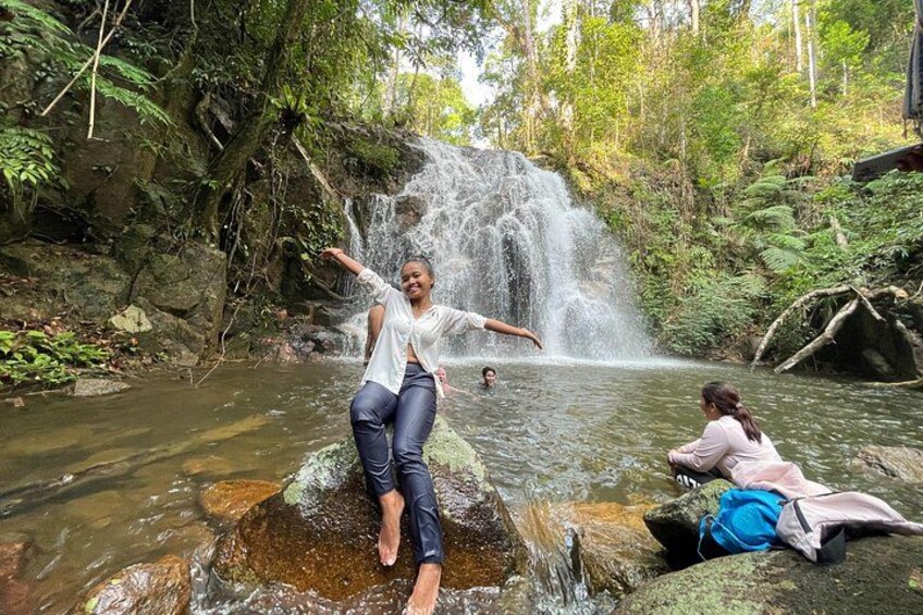 A waterfall, a person standing on a rock, and another person sitting by the water. 3