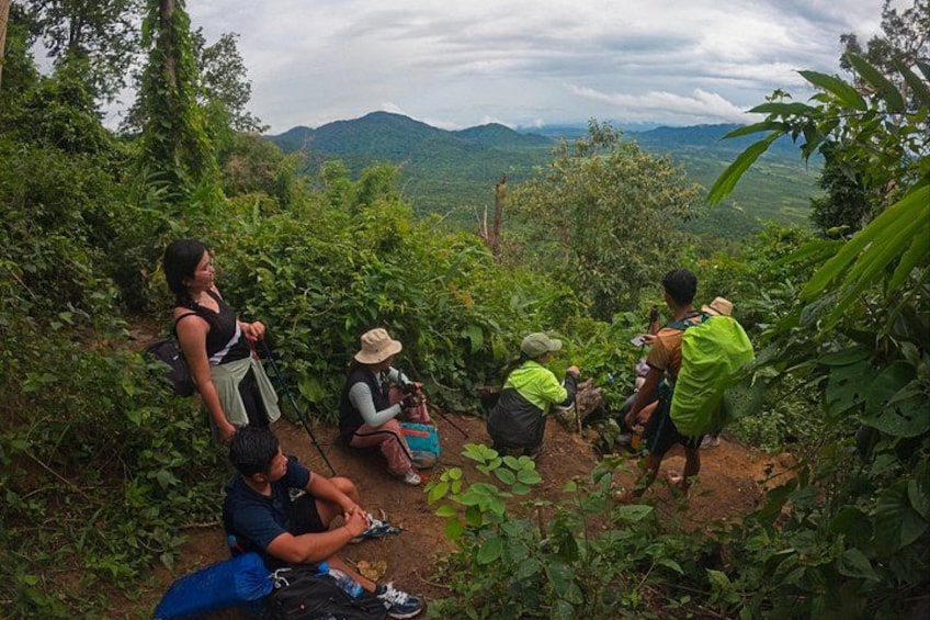 A group of people hiking in a lush, green forest with mountains in the background. 1