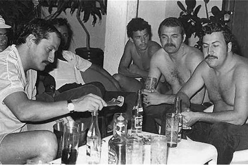 A group of men sitting around a table with bottles and glasses. 2