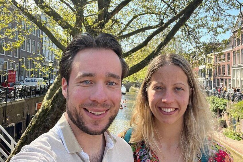 Een stel staat in een gracht, met gebouwen en bomen op de achtergrond. 4