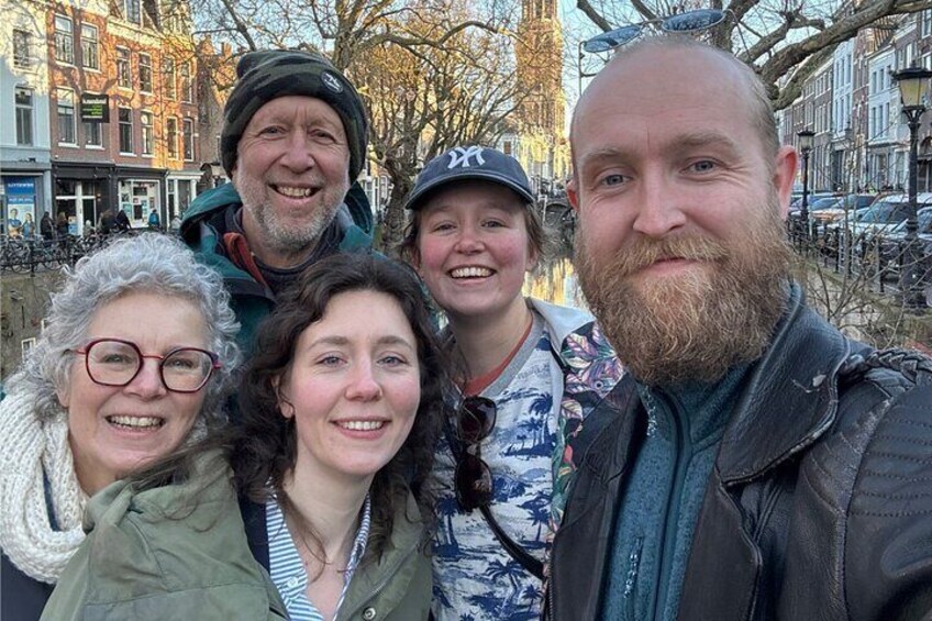 Een groep mensen buiten, in een stedelijke omgeving met gebouwen en een gracht op de achtergrond. 5