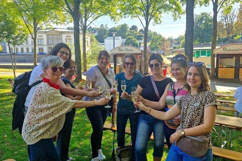 A group of people toasting with drinks in an outdoor setting with trees and buildings in the background. 2