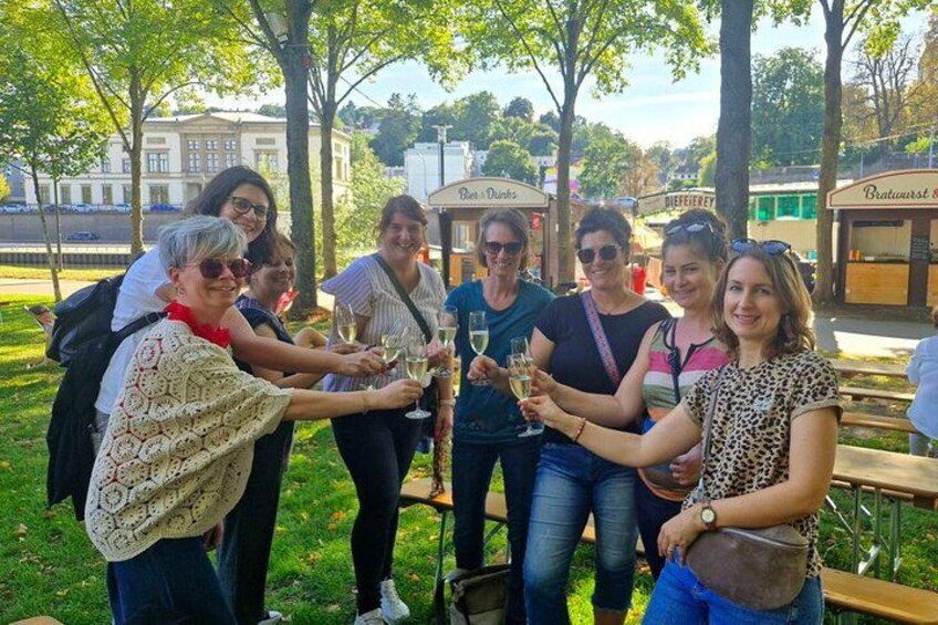 Un grupo de personas brindando con copas de champán en un parque con árboles y un edificio al fondo. 5