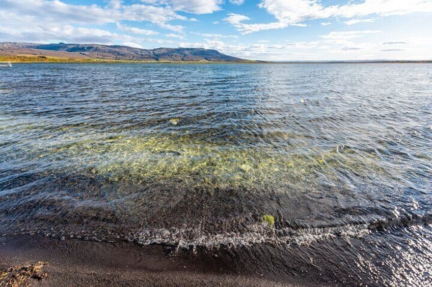 Un lac aux eaux limpides, une plage de sable et, au loin, des montagnes sous un ciel partiellement nuageux. 5