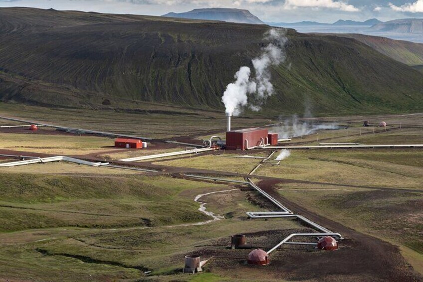 Une centrale géothermique qui produit de la vapeur, entourée de collines douces et d’un petit bâtiment. 4