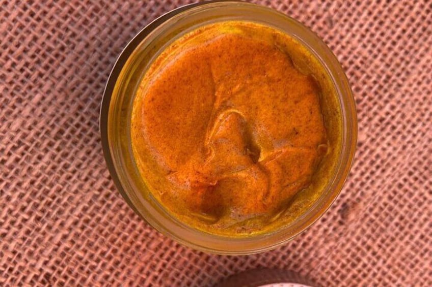 A jar of orange sauce on a textured surface. 1