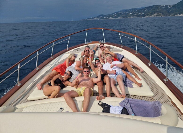 A group of people on a boat with a wooden railing, surrounded by water and distant land. 2