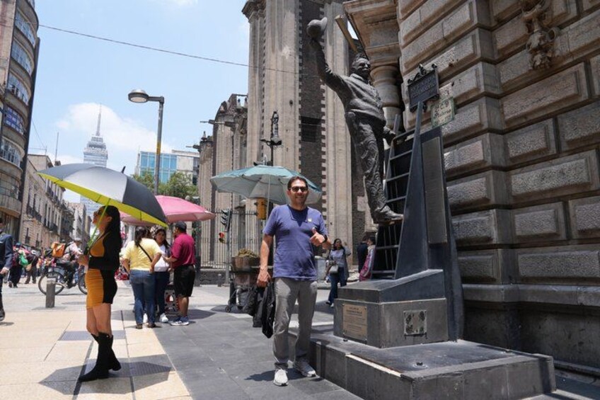 Una concurrida calle urbana con peatones, una estatua y edificios históricos. 5