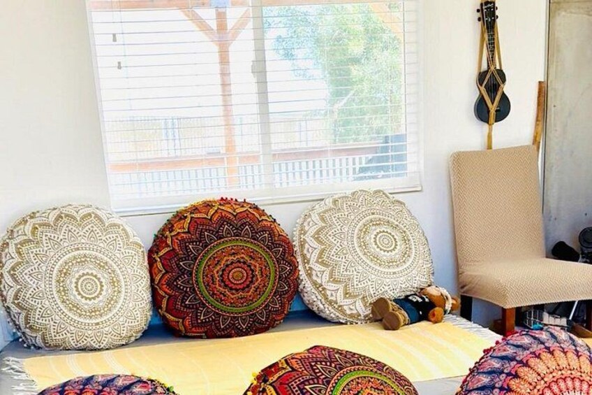 Una habitación con ventana, una guitarra y varios cojines estampados. 3