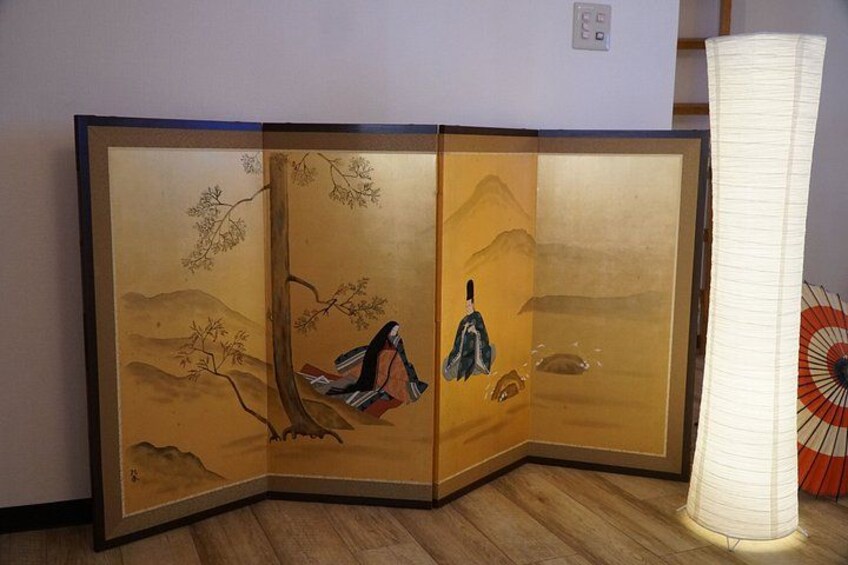 A traditional Japanese room divider with painted scenes, a wooden floor, and a white lamp. 3
