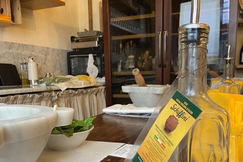 A kitchen counter with a bottle of olive oil, a bowl of greens, and a white ceramic bowl. 2