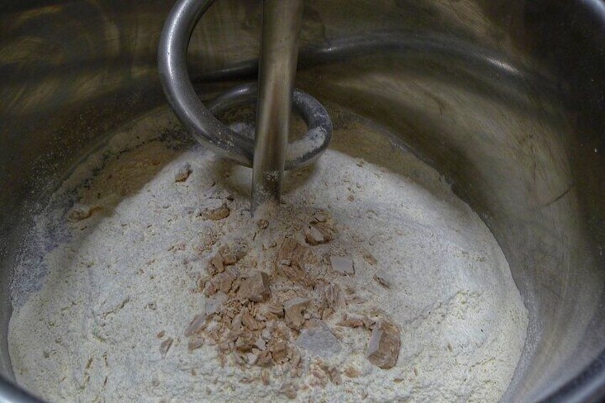 A metal mixing bowl containing flour and oats being stirred by a whisk. 3