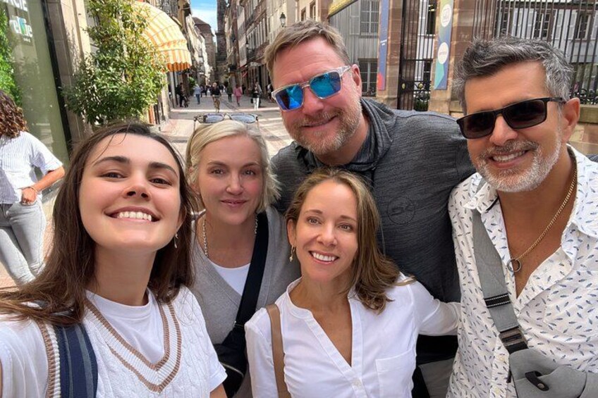 A group of people posing on a city street with buildings and a tree in the background. 2