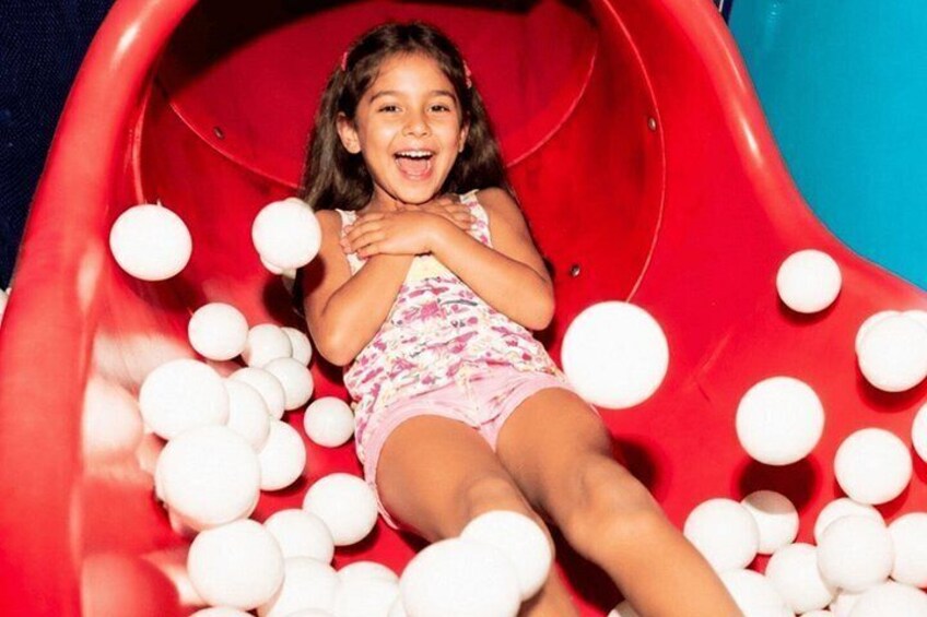 A child sliding down a red slide surrounded by white balls. 1