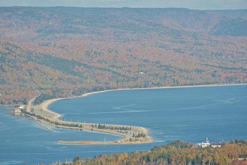 A coastal landscape with a curving shoreline, a lighthouse, and a forested hill in the background. 1