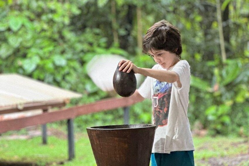Un niño sostiene una olla grande, de pie junto a un recipiente metálico al aire libre. 4