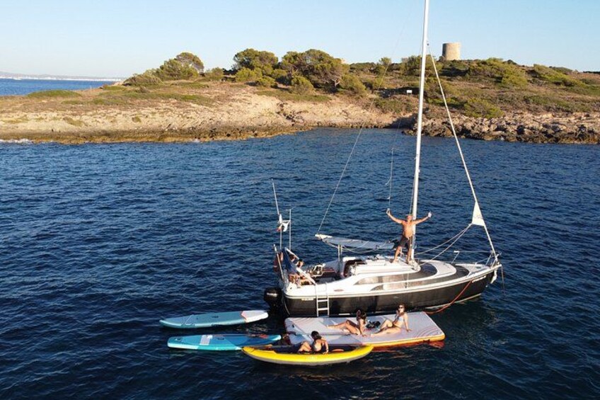 Un velero con personas a bordo, una embarcación más pequeña cerca y una costa rocosa con árboles en el fondo. 4