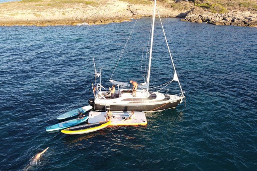 Un velero con un bote auxiliar y una lancha amarrados en una costa rocosa. 3