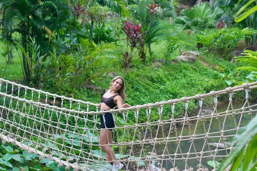 A person crossing a rope bridge in a lush green environment. 3