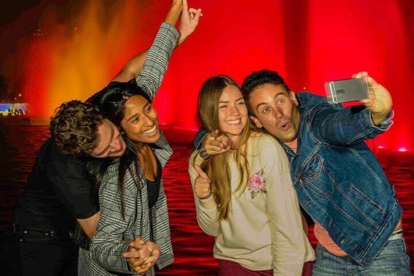A group of people taking a selfie with a red background and a fountain. 2
